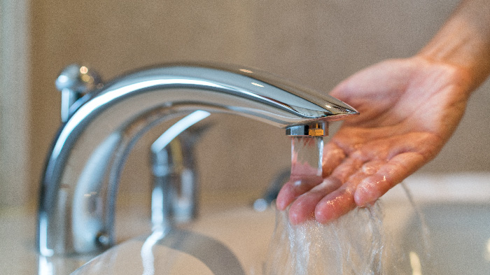 Hand testing water from running faucet